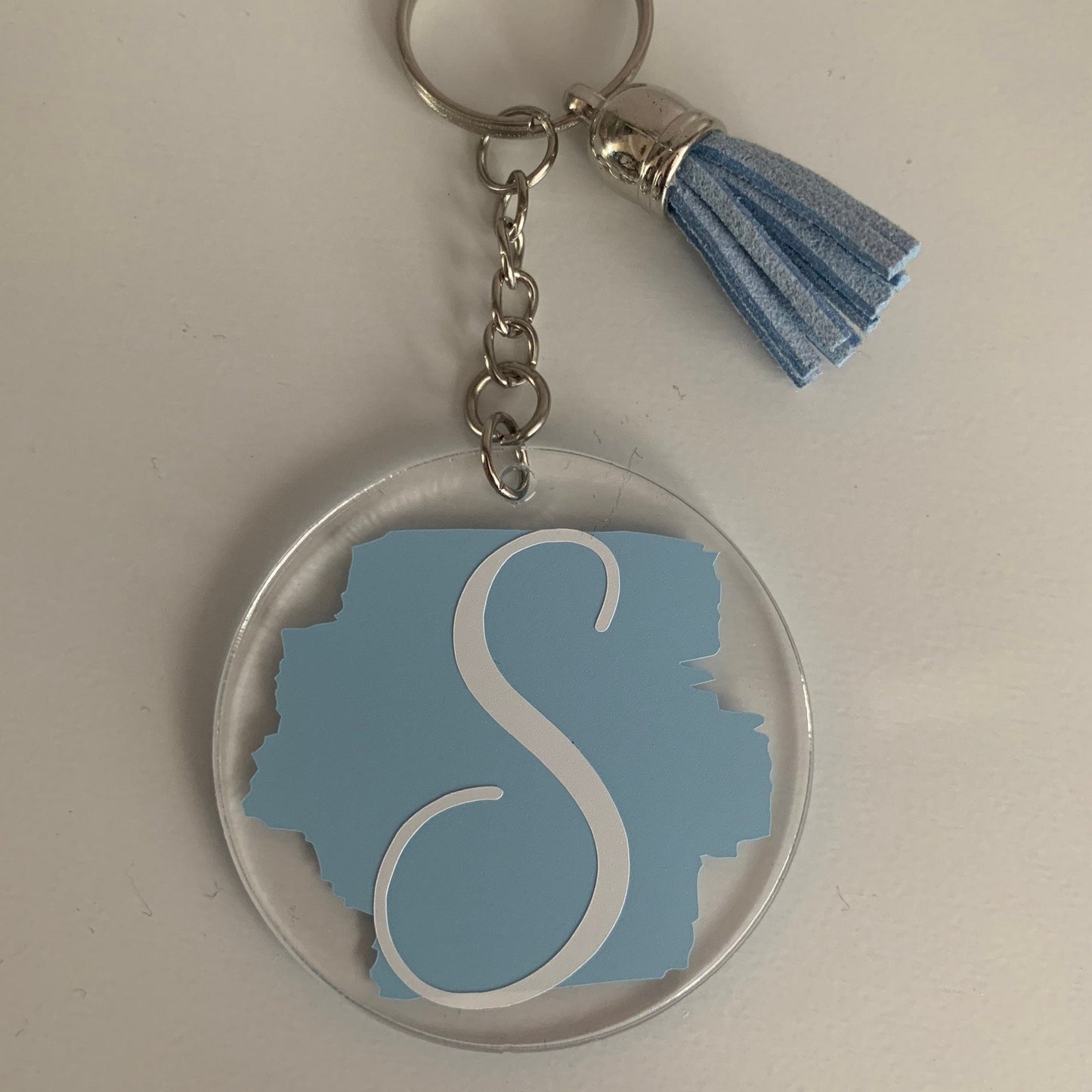 Keychain with blue 'S' design and tassel on a light gray background