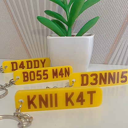 Yellow license plate keychains with text on a white surface with a plant in the background